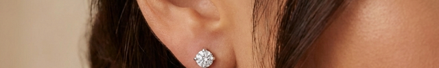 Close-up of a woman wearing an emerald green earring with a diamond top. 