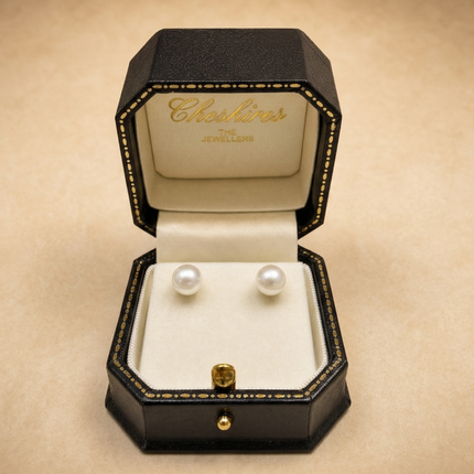 Pair of pearl earrings in a jewellery box on a beige background