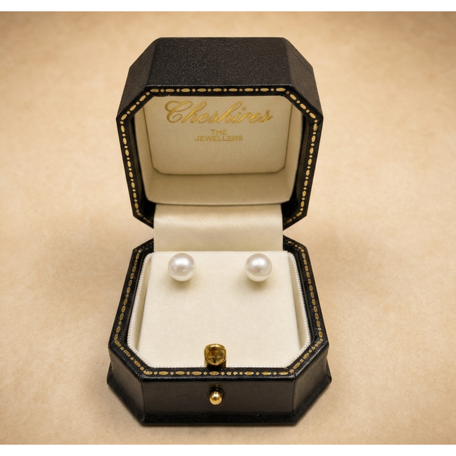 Pair of pearl earrings in a jewellery box on a beige background